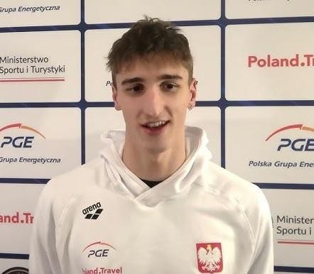 Ksawery Masiuk w trakcie dynamicznego pływania stylem grzbietowym, z widoczną siłą i determinacją, otoczony rozbryzgami wody.