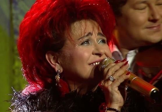Bernadeta Kowalska na scenie z zespołem „Bernadeta Kowalska i Przyjaciele”, śpiewająca z mikrofonem w ręku, w dynamicznym oświetleniu koncertowym.