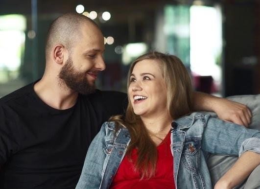 Maciej Pela czule obejmujący swoje dwie córki, w ciepłej, rodzinnej atmosferze domowej, ukazujący ich silną więź.