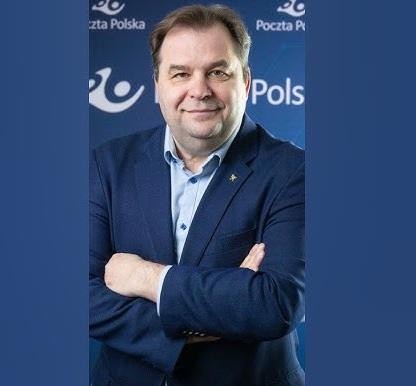 Sebastian Mikosz w dynamicznej pozie w nowoczesnym biurze, gestykulujący, z rozmytym tłem nawiązującym do lotnictwa lub logistyki, symbolizujący aktywne przywództwo.