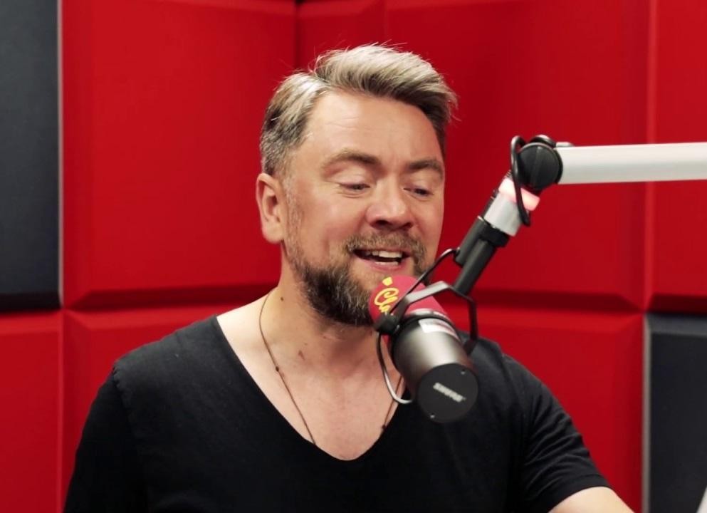 Kuba Badach na scenie podczas koncertu, śpiewający z pasją do mikrofonu, w dynamicznym ujęciu z oświetleniem scenicznym.