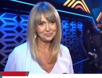 Ewa Wachowicz uśmiechnięta, trzymająca świeżo upieczone ciasto, w tle widoczna nowoczesna kuchnia z elementami kulinarnymi.