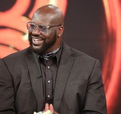 Shaquille O'Neal w koszulce Orlando Magic, w akcji pod koszem, z rozmytym tłem areny koszykarskiej.