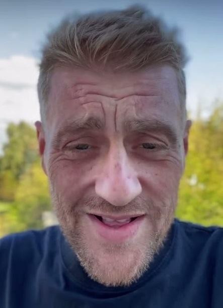 Tomasz Jakubiak przeglądający Instagram na smartfonie, uśmiechnięty, w przytulnym wnętrzu.