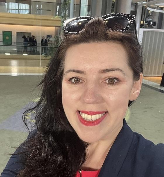 Dominika Ćosić w dynamicznej pozie, na tle sugerującym jej zainteresowania Bałkanami lub działalność pisarską.
