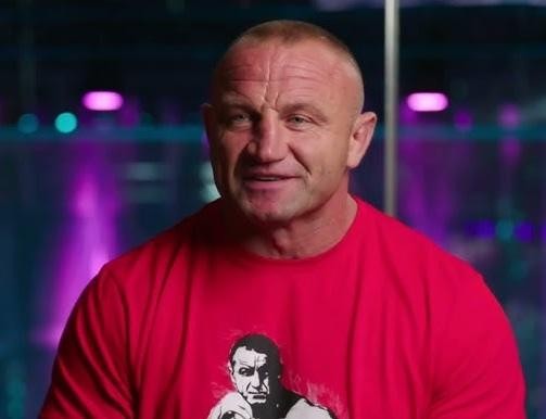 Mariusz Pudzianowski w klatce MMA podczas walki, zadający cios, z widownią w tle, ukazujący dynamikę i siłę zawodnika KSW.